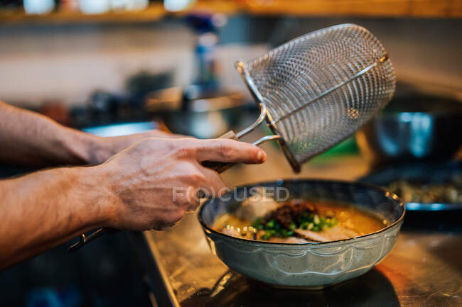 Dall'alto di chef senza volto che cucina il ramen tradizionale con erbe e verdure in caffè — Foto stock