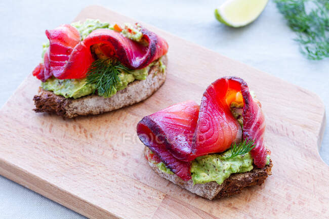 Tasty appetizers of rye bread toasts with avocado spread and smoked salmon slices with dill sprigs on chopping board — Stock Photo