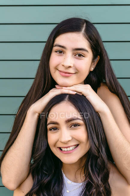 Aufrichtiger weiblicher Teenager lehnt mit den Händen auf dem Kopf von Geschwistern, während er tagsüber in die Kamera schaut — Stockfoto
