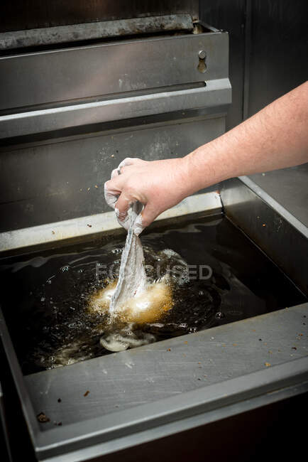 Crop unrecognizable cook preparing fish in oil in deep fryer while cooking in kitchen of restaurant — Stock Photo