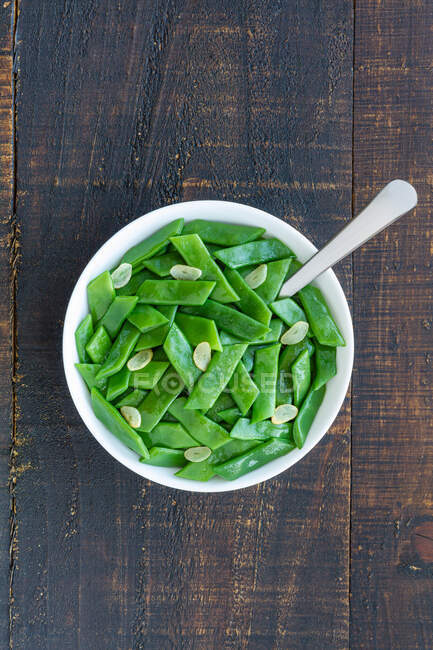 Von oben gesunder Salat mit grünen Bohnen und Knoblauchscheiben in Schüssel auf Holztisch serviert — Stockfoto
