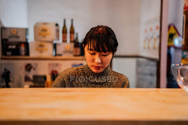 Junge Asiatin in Freizeitkleidung sitzt an der Holztheke, während sie in der Ramen-Bar auf Ordnung wartet — Stockfoto