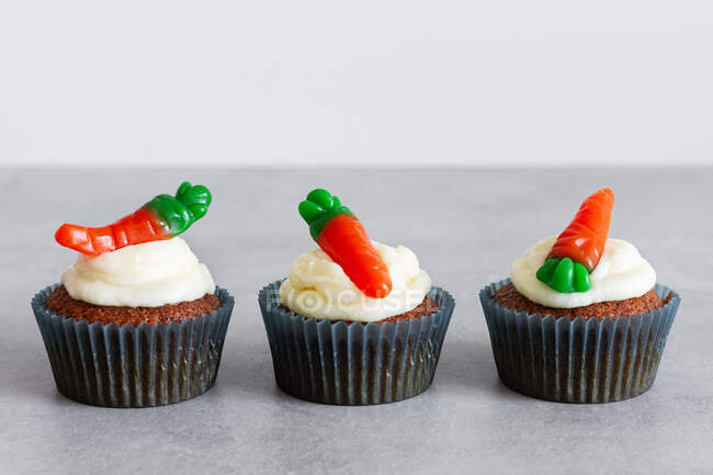 Fileiras de doces deliciosos cupcakes de cenoura com creme macio e gomas em forma de cenoura na superfície cinza — Fotografia de Stock