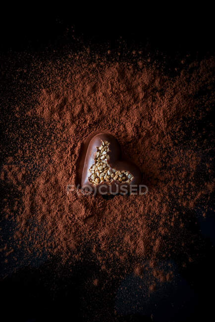 De cima de doces de chocolate em forma de coração com nozes colocadas na mesa com cacau em pó no fundo preto — Fotografia de Stock