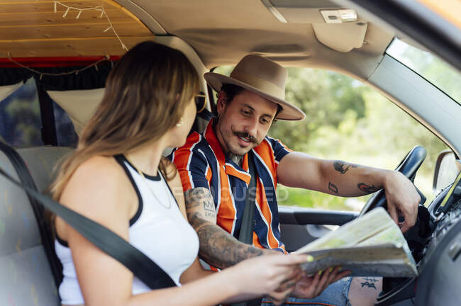 Side view of couple of travelers sitting in van and orientating with paper map during road trip in summer — Stock Photo