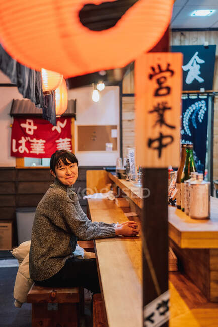 Donna asiatica in abbigliamento casual seduta al bancone in legno in attesa di ordine in ramen bar — Foto stock