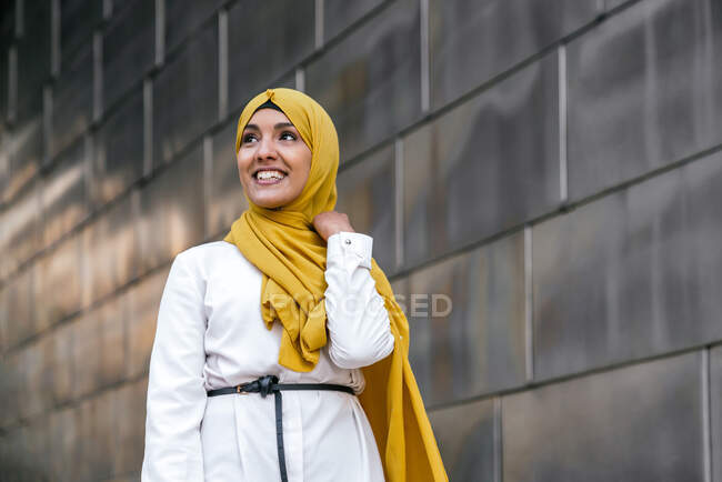 Baixo ângulo de fêmea muçulmana na moda em hijab amarelo em pé na rua e olhando para longe — Fotografia de Stock