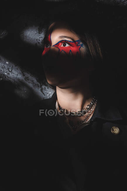 Femme avec ornement créatif autour des yeux regardant loin tout en se tenant dans l'ombre sombre — Photo de stock