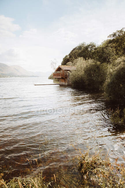 Gemütliches Haus mit Seebrücke am Ufer des plätschernden Sees gegen bewölkten Himmel in der britischen Landschaft — Stockfoto