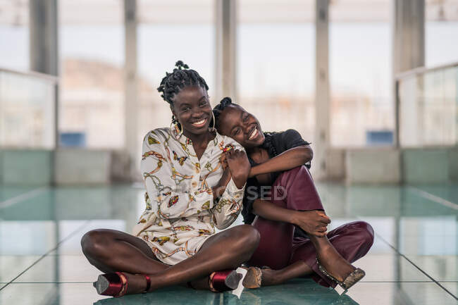 Zufriedene Afroamerikanerinnen, die dicht an dicht sitzen und mit nachdenklichem Lächeln in die Kamera schauen — Stockfoto
