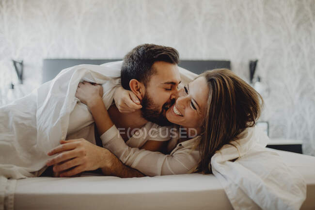 Joyeux jeune homme et femme souriant et câlin tout en étant couchés sur un lit confortable à la maison ensemble — Photo de stock