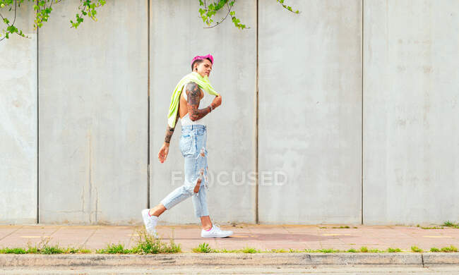 Vue latérale d'un homme gay aux cheveux roses et tatouages marchant dans la rue de la ville en été — Photo de stock