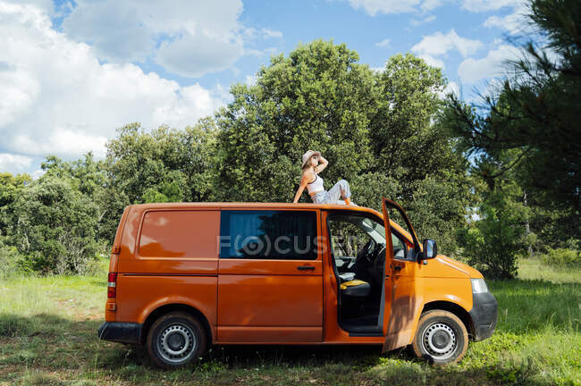 Baixo ângulo de sereno explorador do sexo feminino sentado no telhado da van e desfrutar de aventura de verão no dia ensolarado — Fotografia de Stock