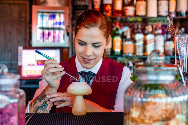 Cheerful female bartender decorating sour cocktail in mushroom shaped glass placed on counter in bar — Stock Photo