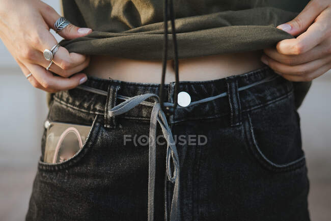 Crop anonymous female in assorted rings showing belly and navel in daytime on blurred background — Stock Photo