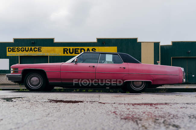 Vista lateral de un coche clásico de color rosa estacionado en la calle en un día lluvioso - foto de stock