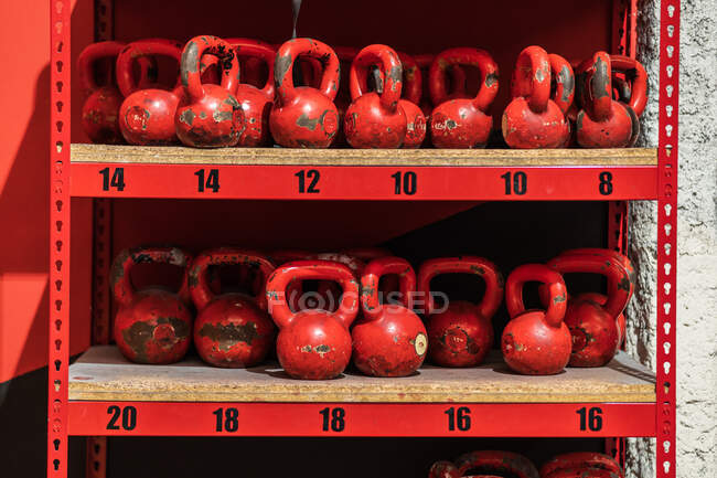 Ensemble de kettlebells rouges minables placés sur une étagère en métal dans une salle de gym contemporaine — Photo de stock