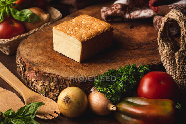 Corte queijo semi macio entre tomates frescos e cebolas na mesa com espátulas e salsa encaracolada — Fotografia de Stock