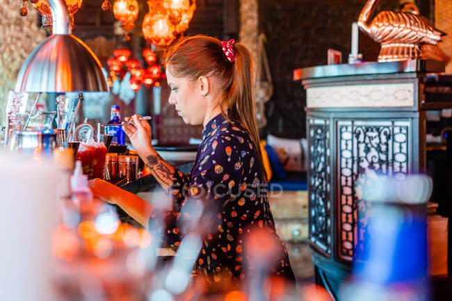 Konzentrierte Barkeeperin garniert frische Cocktails in Gläsern, die in der Bar auf dem Tresen stehen — Stockfoto