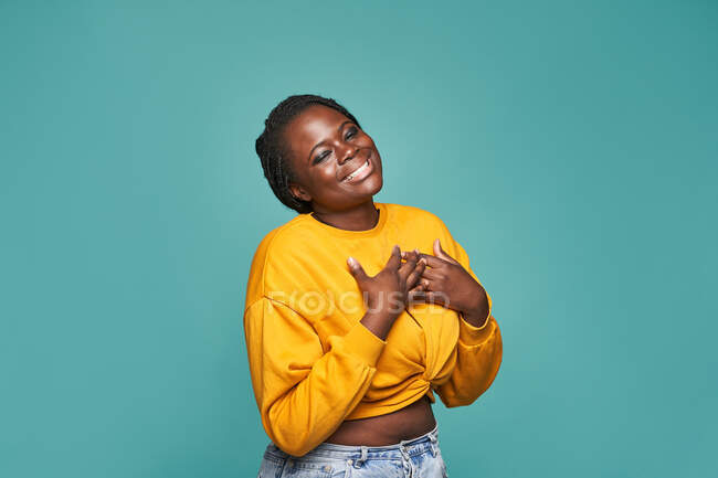 Cheerful African American female in trendy yellow clothes dancing happily against blue background in studio — Stock Photo
