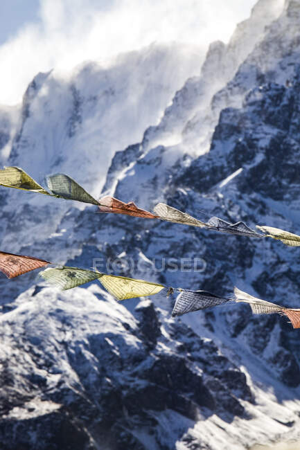 Rows of colorful Buddhist prayer flags hanging on ropes on background of rocky Himalayas covered with snow in winter in Nepal — Stock Photo