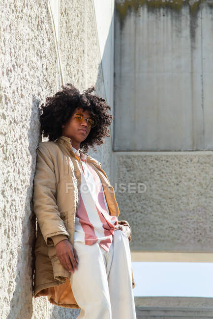 From below African American male in vintage coat and sunglasses with Afro hairstyle standing on stairs while looking away — Stock Photo