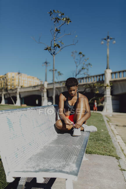 Junge, fitte Afroamerikanerin ruht sich aus und bindet die Schnürsenkel, nachdem sie Sport auf der Parkbank gemacht hat — Stockfoto
