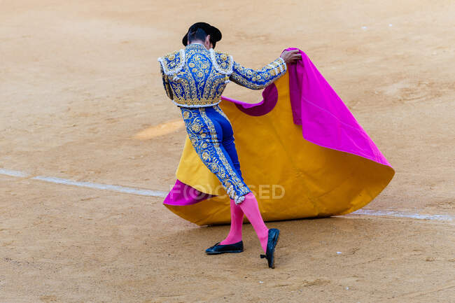 Vista posteriore del torero anonimo in costume tradizionale luminoso e con mantello che si esibisce su arena sabbiosa durante il festival corrida — Foto stock
