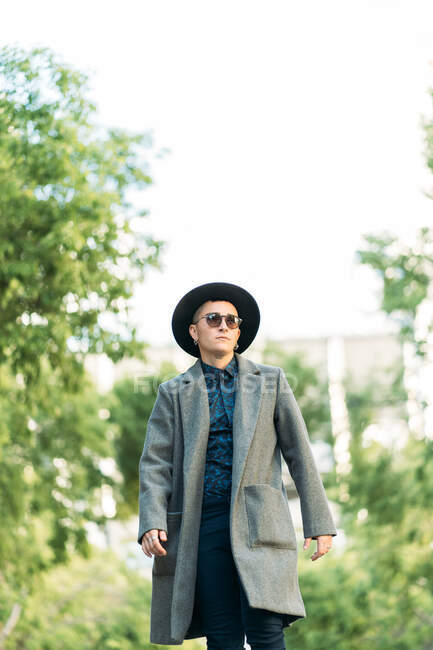 Jeune transgenre en manteau et chapeau classe regardant loin en plein jour — Photo de stock