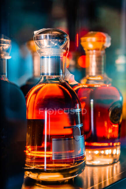 Прозрачные стеклянные бутылки с виски, помещенные на прилавок в темном баре ночью — стоковое фото
