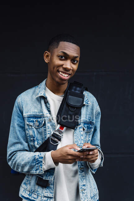 Front view of a young black man with mobile and backpack on the street — Stock Photo