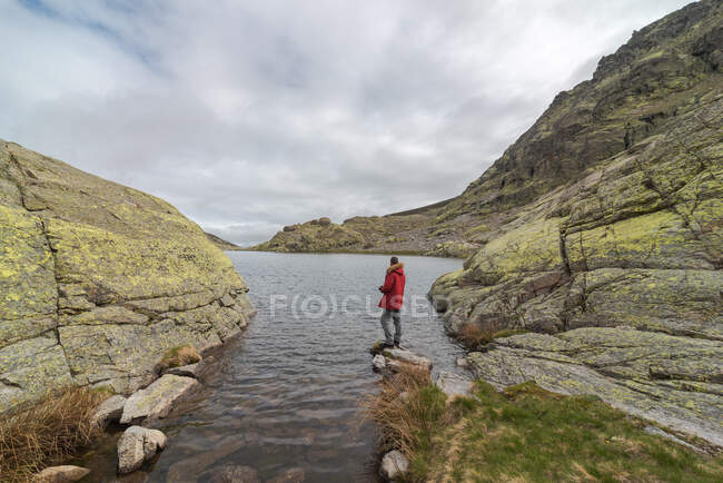 Vista laterale dell'uomo anonimo in capispalla in piedi su pietre vicino al lago Laguna Grande tra le montagne della Sierra de Gredos a Avila, Spagna — Foto stock