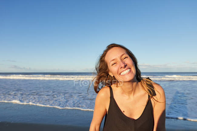 Smiling female in summer dress standing on sandy seashore and looking at camera — Stock Photo