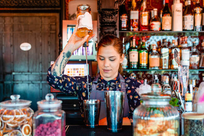 Barman femelle versant de l'alcool dans shaker tout en préparant un cocktail rafraîchissant au comptoir dans le bar et regardant ailleurs — Photo de stock