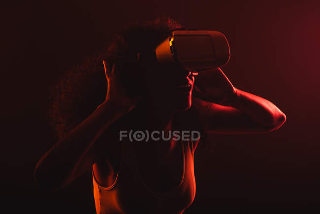 Анонімні дивовижні етнічні жінки з відкритим ротом досліджують віртуальну реальність в гарнітурі на чорному тлі — стокове фото