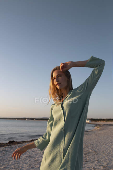 Femme blonde aux cheveux longs debout sur la plage regardant loin — Photo de stock