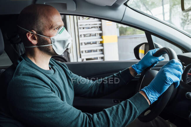 Вид збоку серйозної людини з використанням захисної маски водіння автомобіля під час карантину — стокове фото