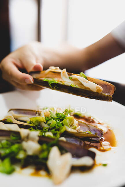 Mão de fêmea anônima segurando amêijoa navalha deliciosa enquanto come no restaurante — Fotografia de Stock