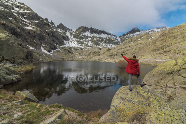 Vista posterior del hombre anónimo en ropa de abrigo de pie sobre piedras cerca del lago Laguna Grande en medio de las montañas de la Sierra de Gredos en Ávila, España - foto de stock