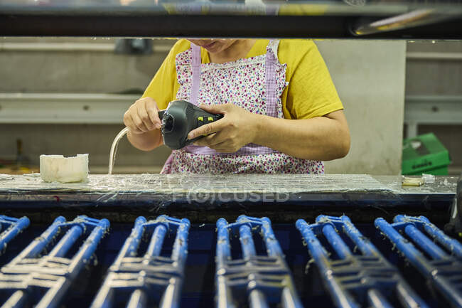 Detalle del trabajador que aplica pegamento a la suela de los zapatos en una línea de producción de fábrica de zapatos chinos - foto de stock