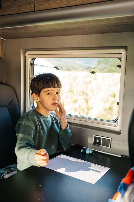 Little boy sitting inside a motorhome while doing his homework and looking at camera — Stock Photo