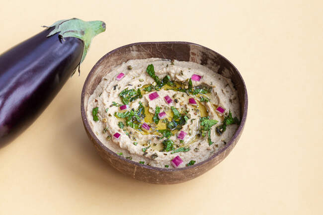 Beringela madura fresca colocada na mesa bege com uma tigela de delicioso prato tradicional de Baba ghanoush — Fotografia de Stock