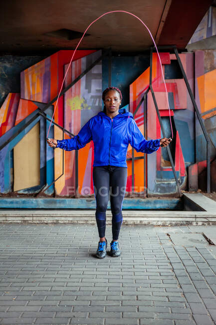 Атлетическая этническая женщина, стоящая на улице и упражняющаяся с скакалкой — стоковое фото