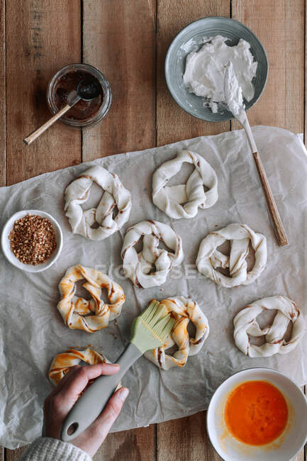 Vue du dessus d'une personne méconnaissable étalant des œufs crus sur des bretzels avec de la confiture de figue et du fromage à la crème sur une table en bois — Photo de stock