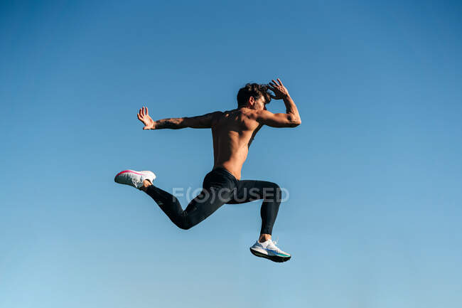 Vista lateral do atleta masculino ativo em roupas esportivas pulando durante o treinamento cardio na luz solar — Fotografia de Stock