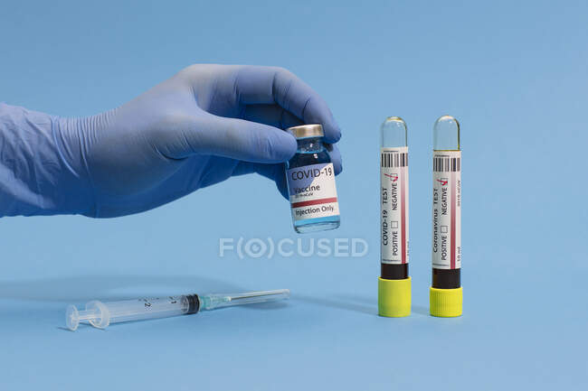 Vaccino per coronavirus in matraccio vicino alla siringa con ago e esame del sangue negativo su fondo blu — Foto stock