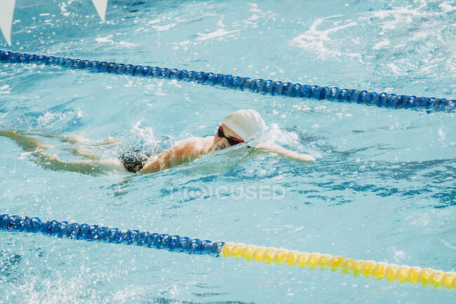 Vista lateral do atleta paralímpico em óculos e boné sem mão nadando rastejar estilo na piscina entre as pistas — Fotografia de Stock
