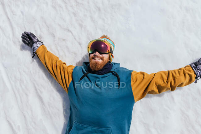 Vista superior do atleta masculino barbudo com barba em óculos esportivos deitado na neve de Sierra Nevada, na Espanha — Fotografia de Stock