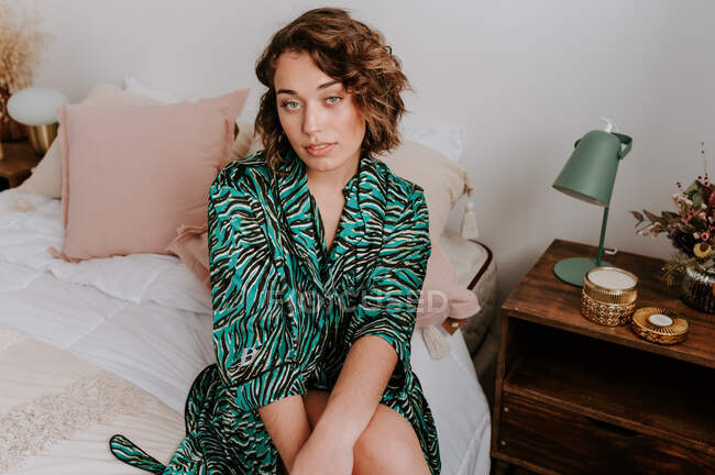 Hohe Winkel der ruhigen Frau in häuslicher Kleidung ruht auf weichem Bett zu Hause und blickt in die Kamera — Stockfoto