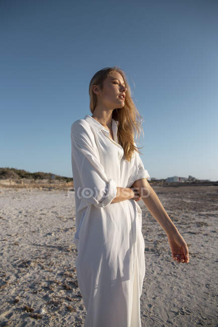 Mulher loira com cabelos longos em pé na praia olhando para longe — Fotografia de Stock
